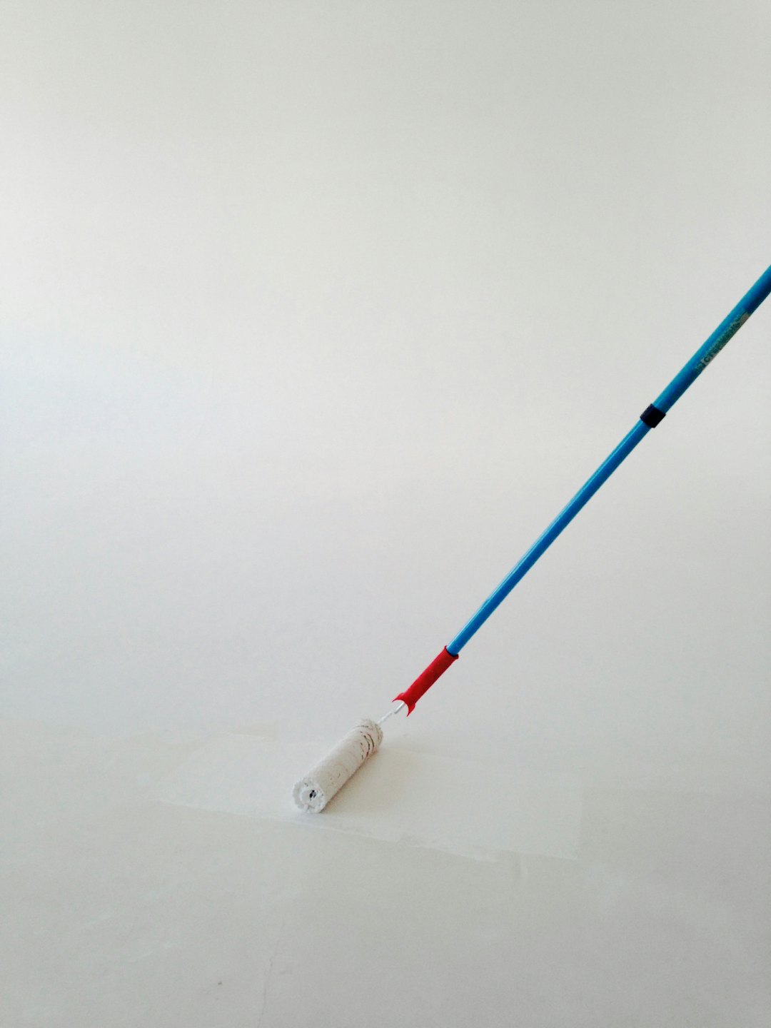 Een muur schilderen met een roller met blauw en rood handvat.