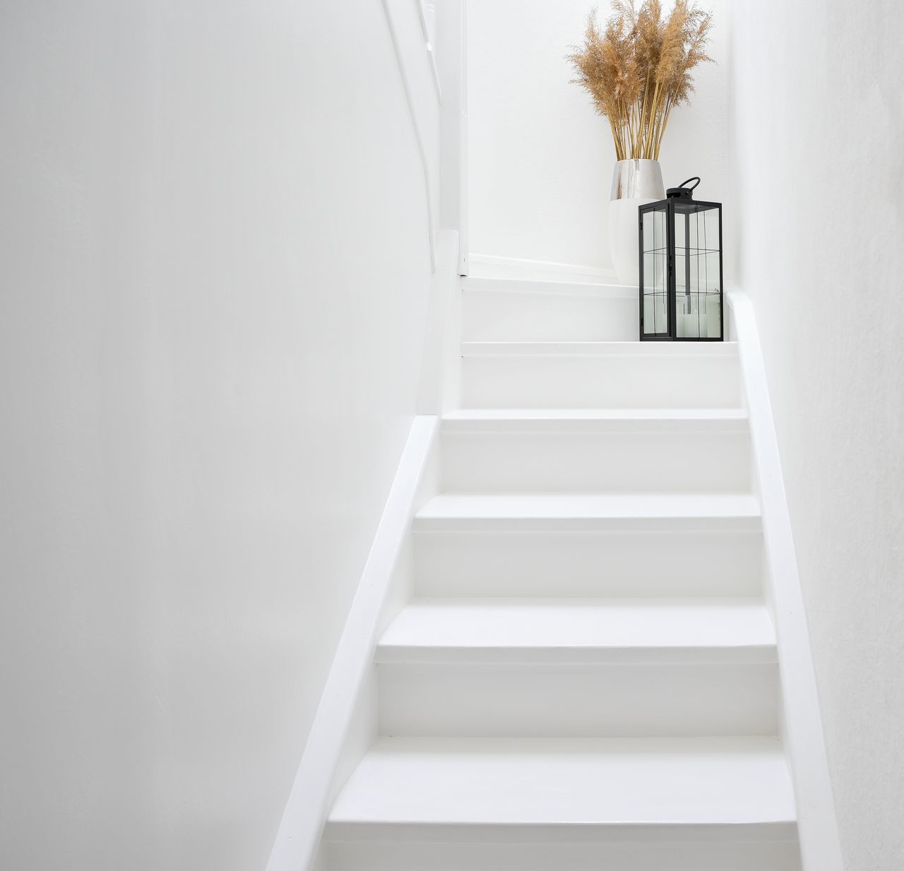 Bright and modern Scandinavian-style staircase with a glass lantern and dried plants.