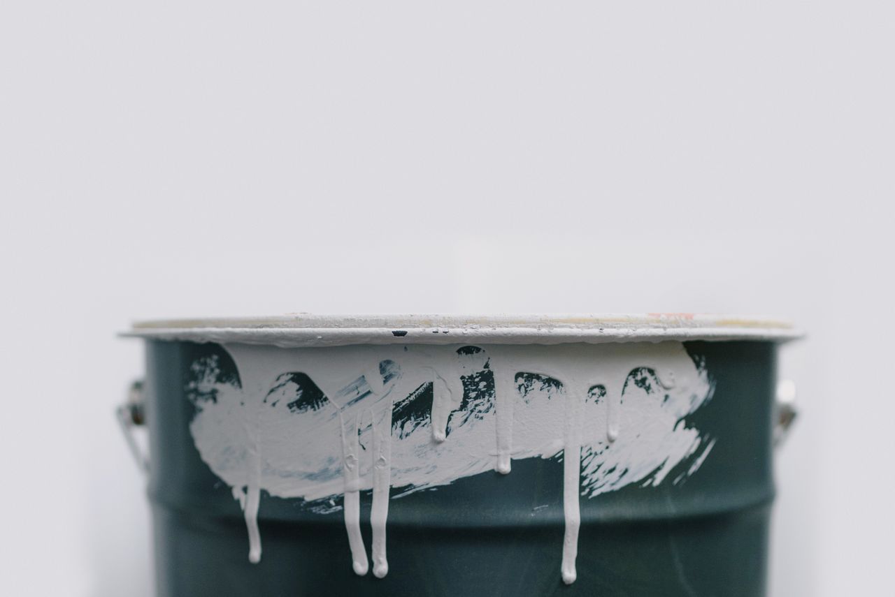 Closeup of white drips from paint on green metal bucket during repair at home